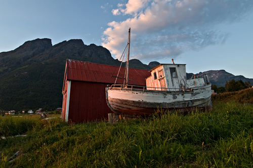 Photo of an old boat being lightened by a red sunset against a magnificent mountain