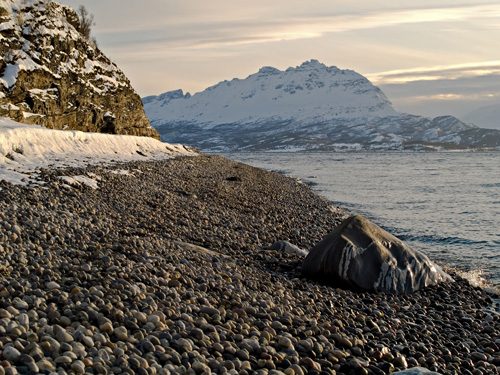 Photo of pebble beach and a mountain covered in snow