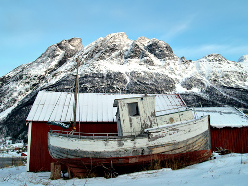 Photo of old fishing boat against old snow filled mountain in northern Norway